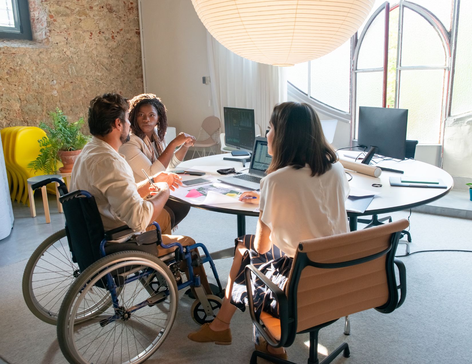 3 individuals sitting at board room table discussing a business plan one male in a wheelchair